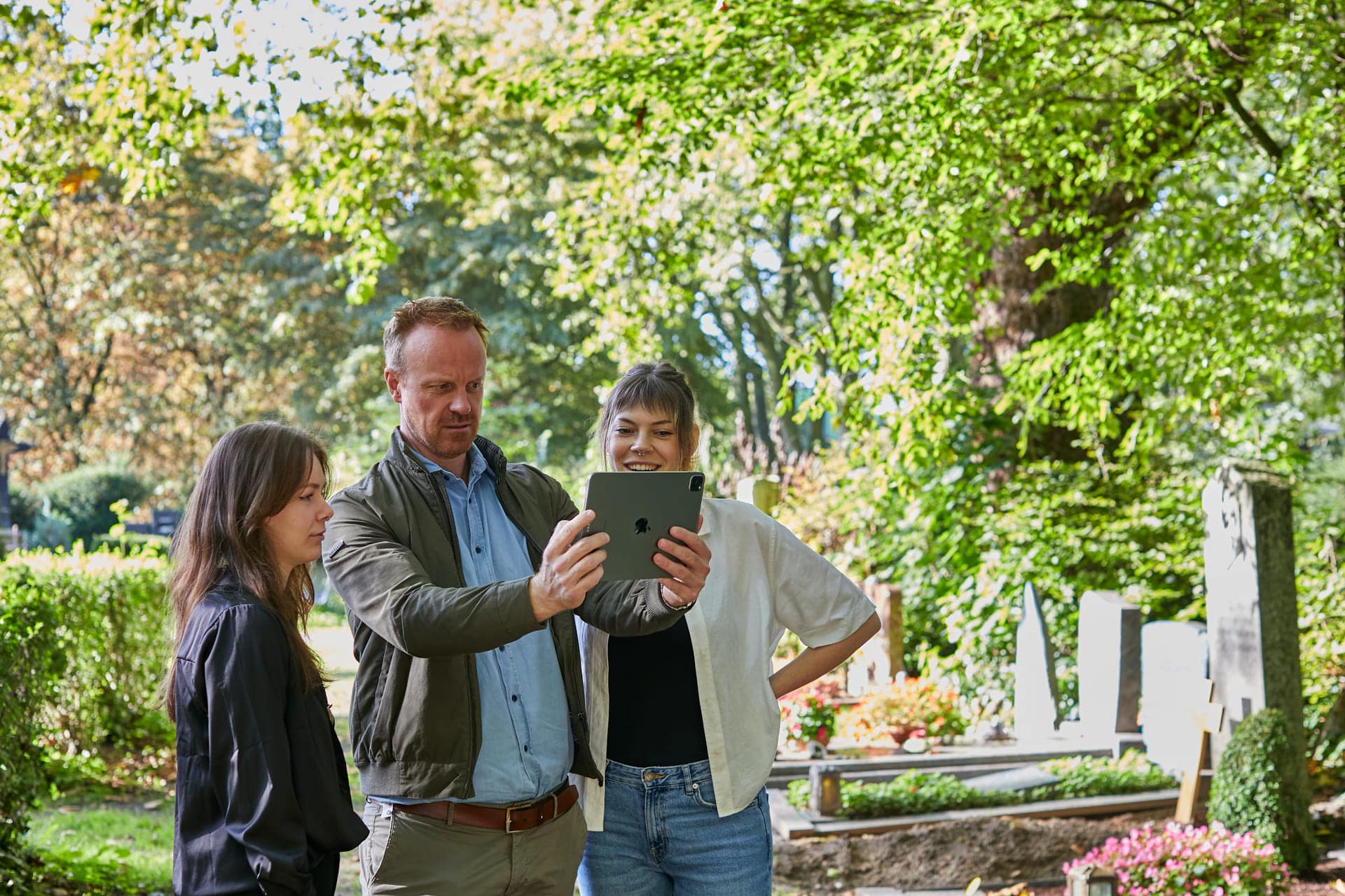 Drei Personen, die mit dem digitalen Friedhofsplan auf dem Friedhof stehen