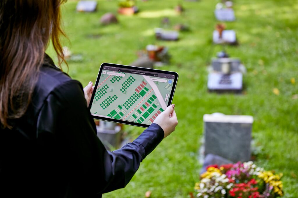 Der digitale Friedhofsplan wird in den Händen auf dem Friedhof gehalten.